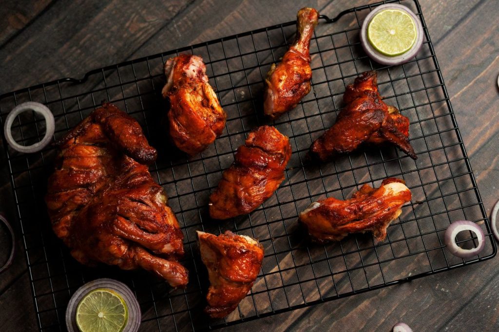 Home Tasty grilled chicken pieces on a wire rack with onion and lime garnishes.
